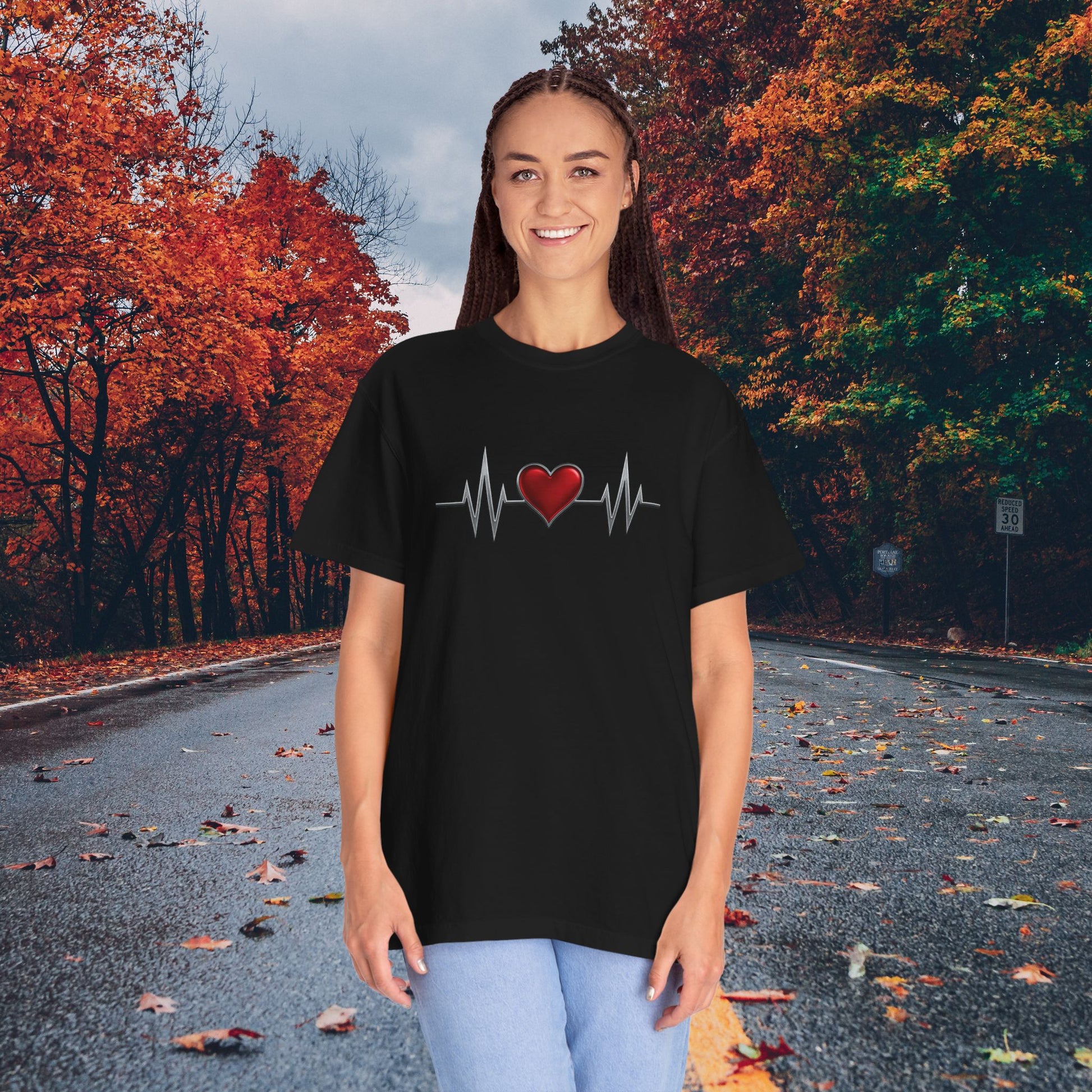 Black heart graphic t-shirt with red heart and heartbeat design worn by woman on autumn road