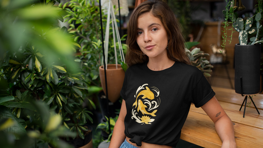 Woman wearing black koi fish graphic tee with yellow koi fish design sitting among indoor plants